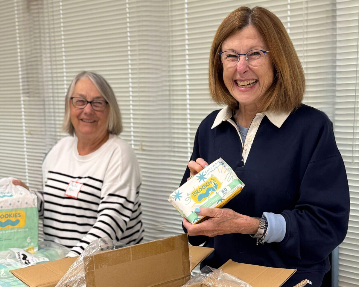 Two volunteers smiling while sorting boxes of baby wipes for distribution