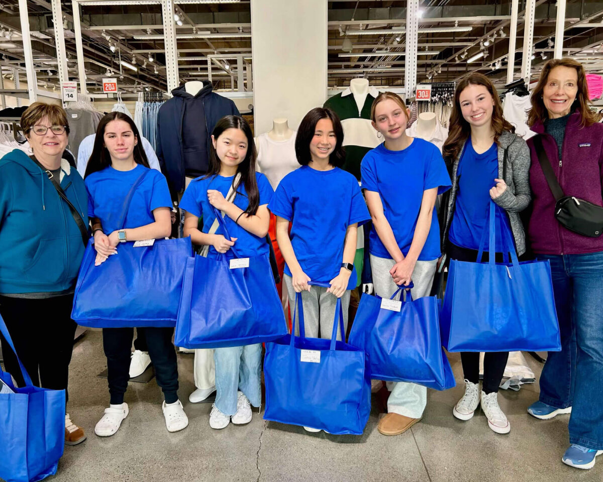 Group of teen volunteers in matching blue shirts holding shopping bags at the Common Threads clothing store