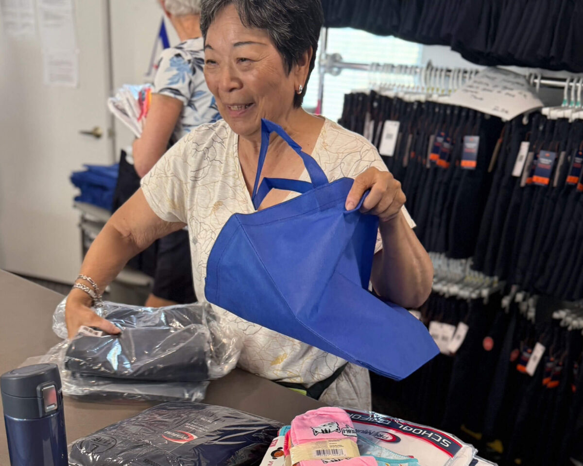 Volunteer assembling elementary school uniforms into blue tote bags for distribution