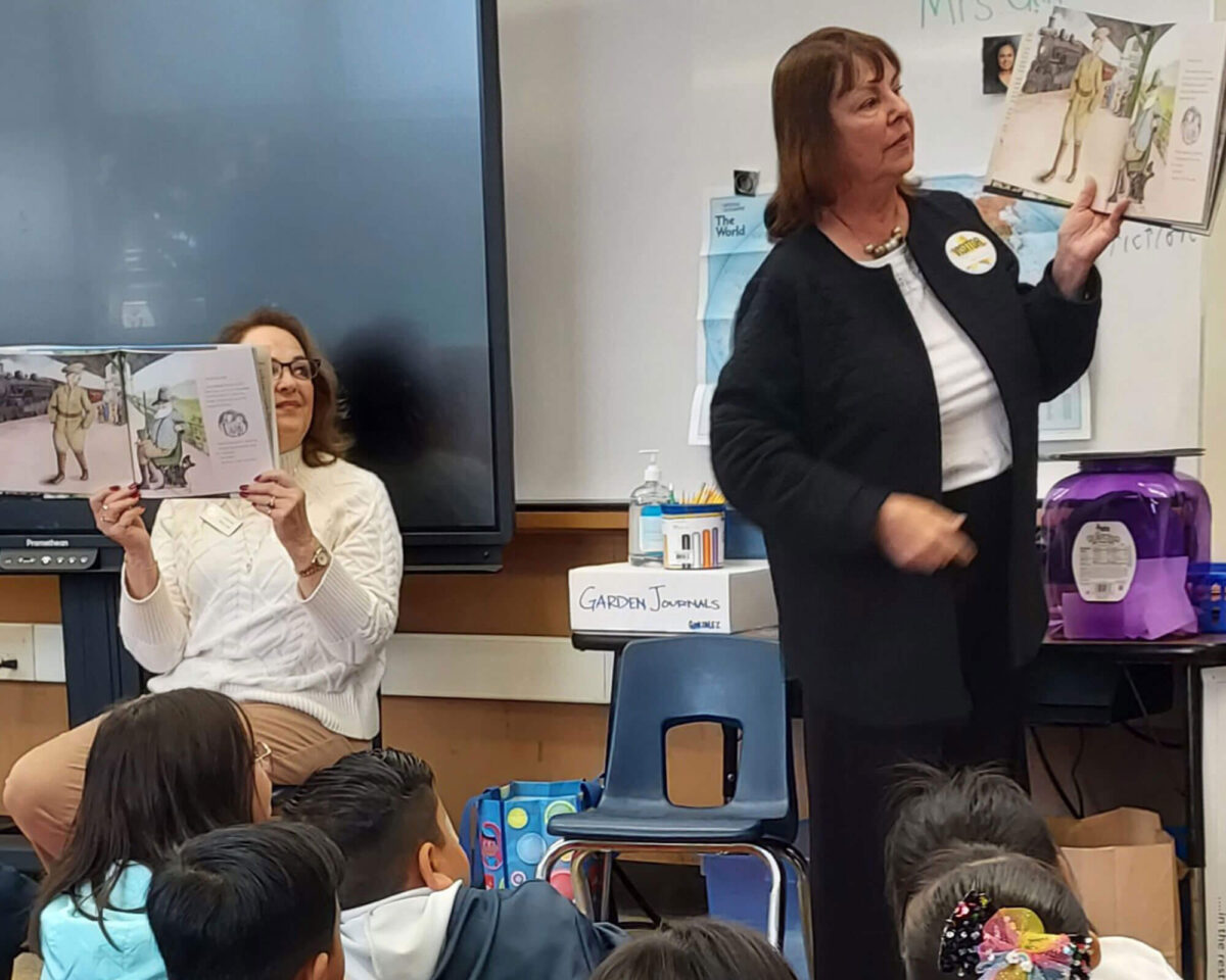 Two volunteers presenting picture books to elementary students during a READ program classroom visit