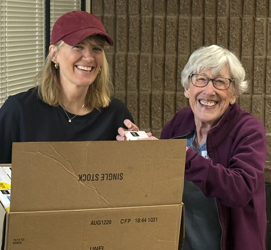 Two volunteers smiling behind cardboard food-donation boxes at a packing event
