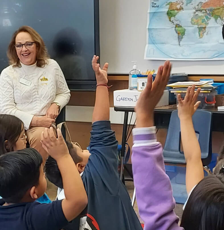 Volunteer teaching elementary students who eagerly raise their hands in a classroom