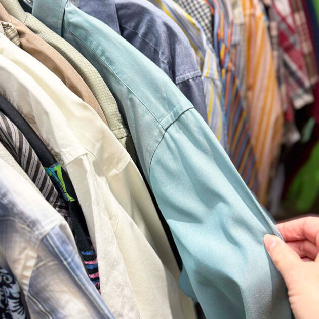 Shopper browsing a rack of gently-used men's button-down shirts at the Giving Partners Thrift Shop