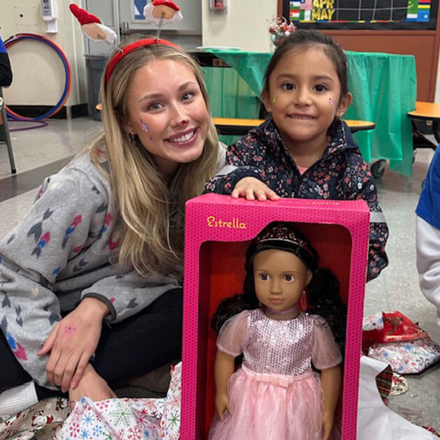 Volunteen smiling with a young child receiving an Estrella doll at a holiday gift-giving event