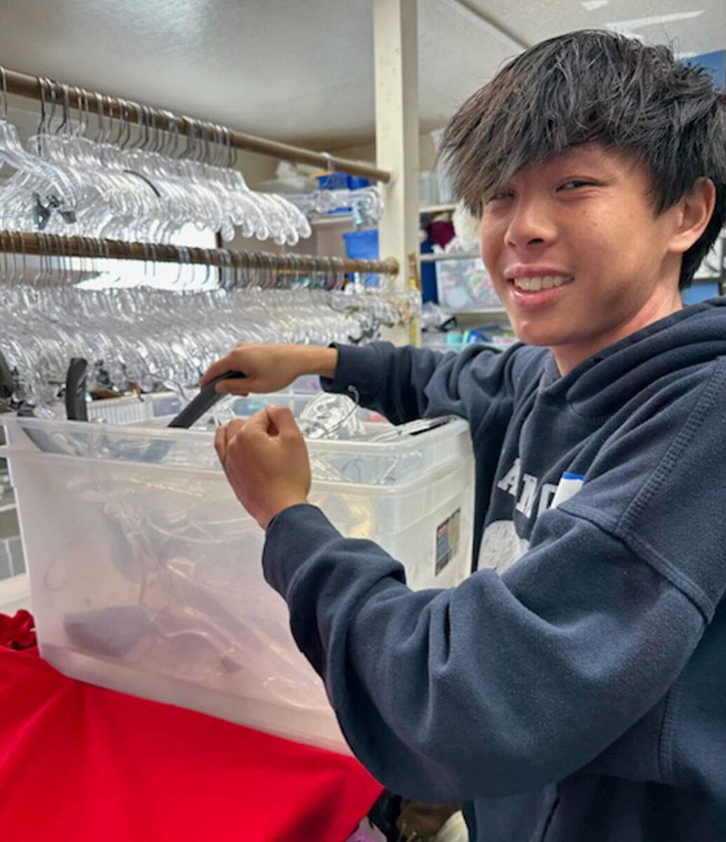 Volunteen smiling while organizing plastic hangers in a storage bin at the thrift shop
