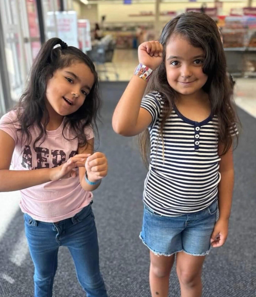 Two young girls smiling and showing off princess-themed wristbands at the Giving Partners Thrift Shop